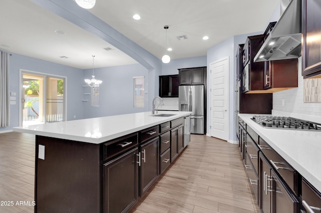 kitchen with visible vents, a sink, stainless steel appliances, wall chimney exhaust hood, and light countertops