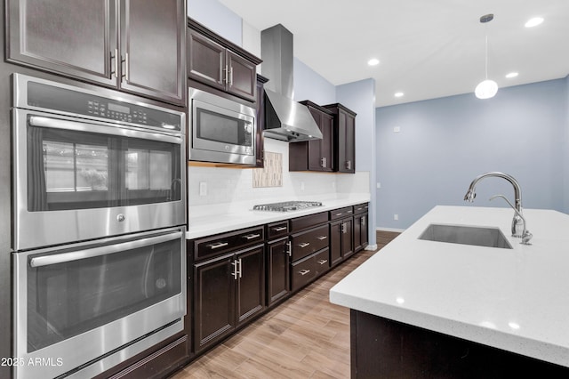 kitchen with light wood finished floors, a sink, stainless steel appliances, wall chimney exhaust hood, and backsplash