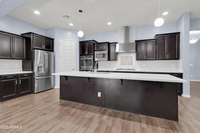 kitchen with visible vents, a sink, stainless steel appliances, light countertops, and wall chimney exhaust hood