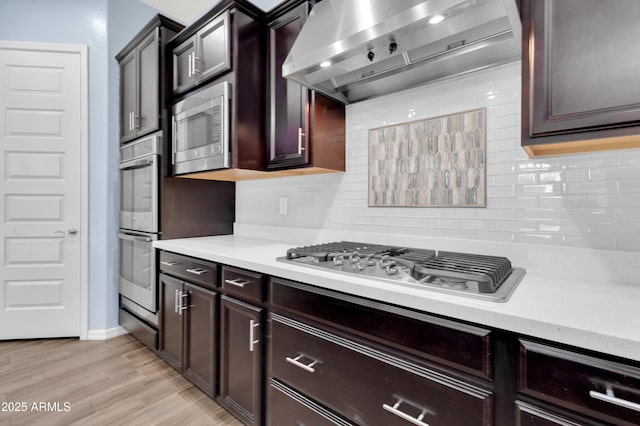 kitchen featuring decorative backsplash, appliances with stainless steel finishes, light countertops, and wall chimney range hood