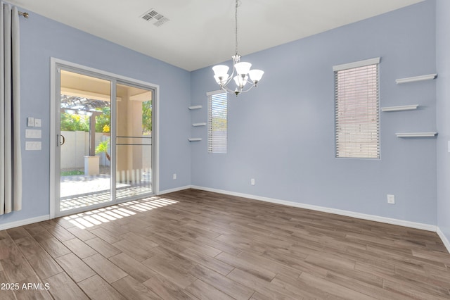 empty room featuring an inviting chandelier, wood finished floors, visible vents, and baseboards