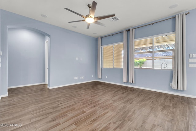 empty room with wood finished floors, baseboards, visible vents, arched walkways, and ceiling fan