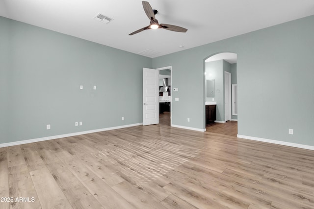 interior space with visible vents, baseboards, light wood-type flooring, arched walkways, and a ceiling fan