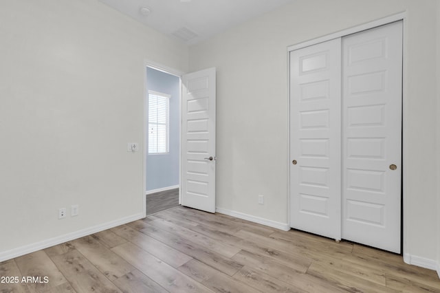 unfurnished bedroom with a closet, baseboards, and light wood finished floors