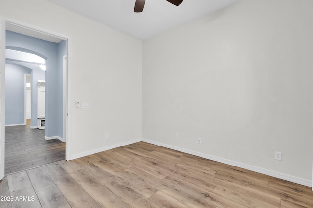 empty room featuring baseboards, arched walkways, wood finished floors, and a ceiling fan