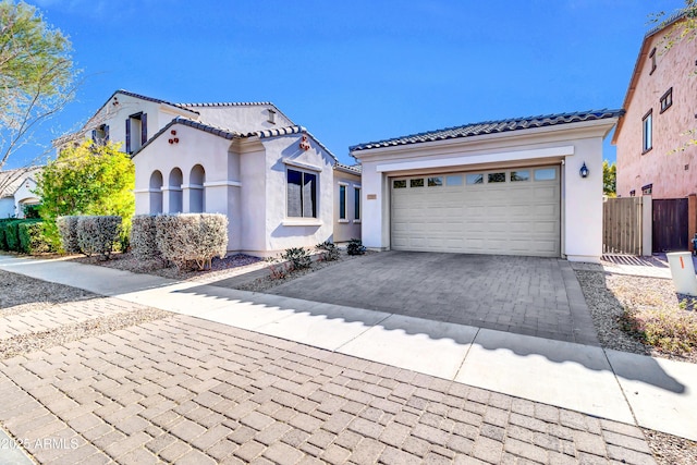 mediterranean / spanish-style house featuring fence, stucco siding, a garage, a tiled roof, and decorative driveway