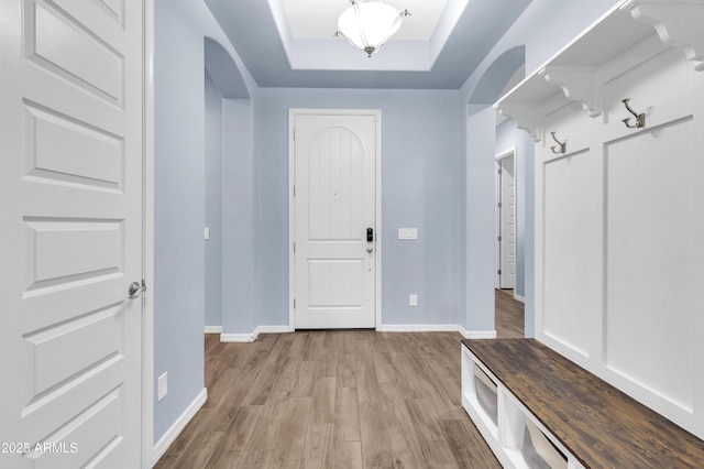 mudroom featuring light wood-style floors, arched walkways, a raised ceiling, and baseboards