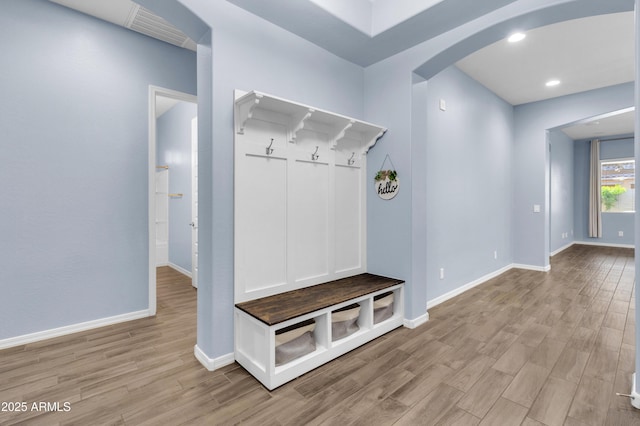 mudroom featuring visible vents, arched walkways, light wood-style floors, and baseboards