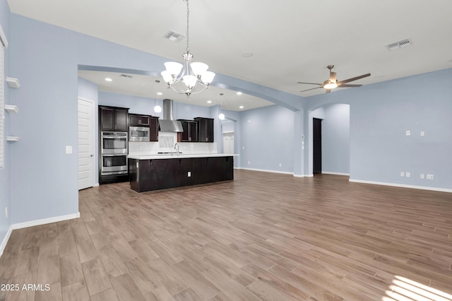 kitchen with open floor plan, wall chimney range hood, arched walkways, and visible vents