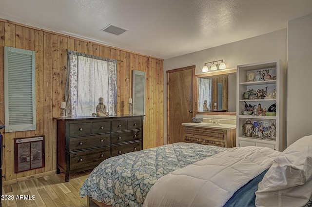 bedroom with wooden walls, sink, light hardwood / wood-style floors, and heating unit