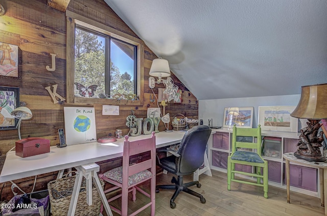 home office with vaulted ceiling, light wood-type flooring, a textured ceiling, and wooden walls