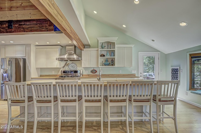 kitchen featuring wall chimney exhaust hood, a breakfast bar area, white cabinetry, stainless steel fridge, and stove