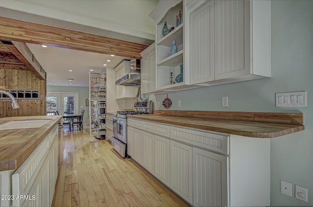 kitchen featuring wood counters, sink, white cabinets, wall chimney range hood, and stainless steel gas range