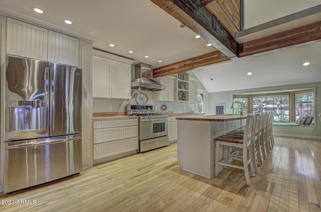 kitchen featuring appliances with stainless steel finishes, vaulted ceiling with beams, a center island, light hardwood / wood-style floors, and wall chimney exhaust hood