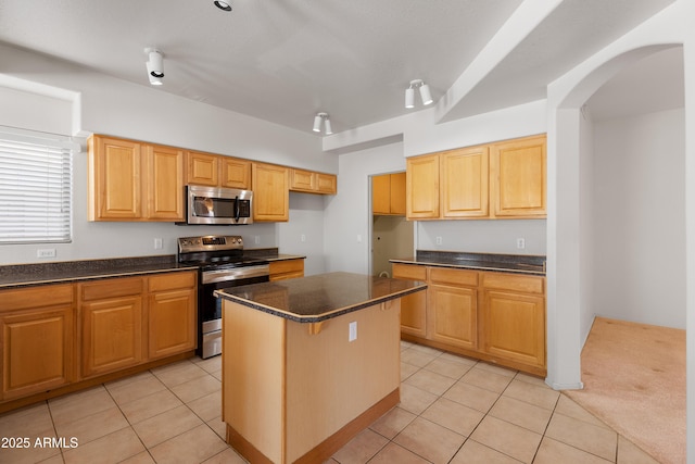 kitchen featuring arched walkways, stainless steel appliances, light tile patterned flooring, and a center island