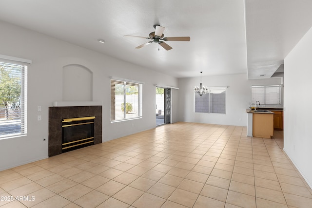 unfurnished living room with a tile fireplace, light tile patterned flooring, a sink, and ceiling fan with notable chandelier