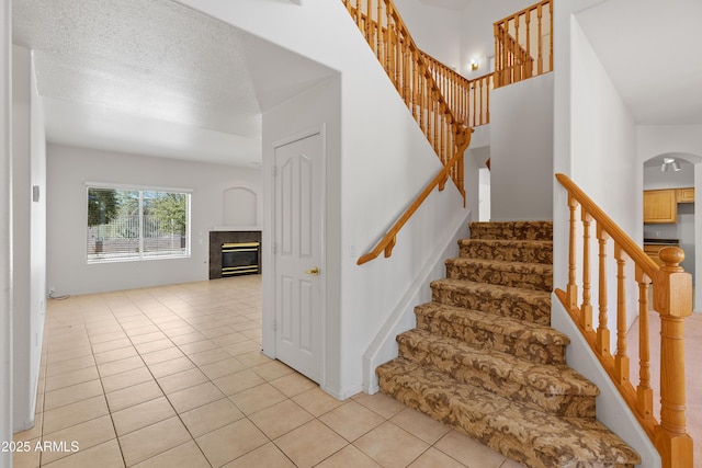 stairs featuring arched walkways, a textured ceiling, a tiled fireplace, and tile patterned floors