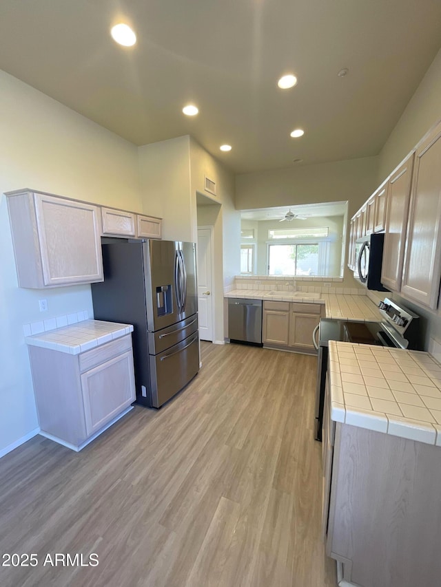 kitchen featuring tile counters, light hardwood / wood-style floors, ceiling fan, and appliances with stainless steel finishes