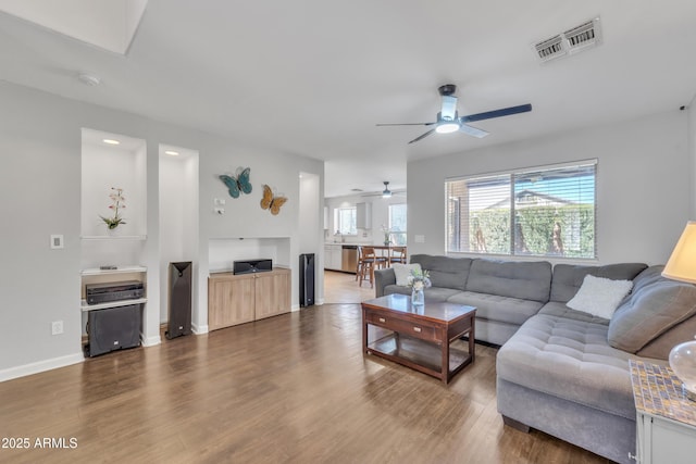 living area with visible vents, ceiling fan, baseboards, and wood finished floors