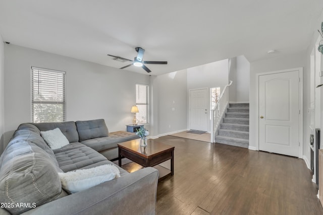 living area featuring a ceiling fan, a healthy amount of sunlight, wood finished floors, and stairs