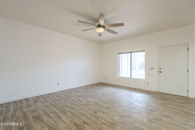 spare room featuring a ceiling fan, light wood-type flooring, and baseboards