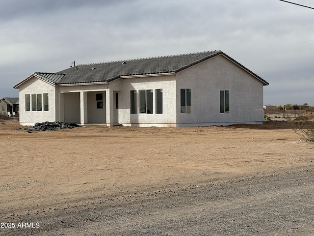 rear view of property featuring a tile roof and stucco siding