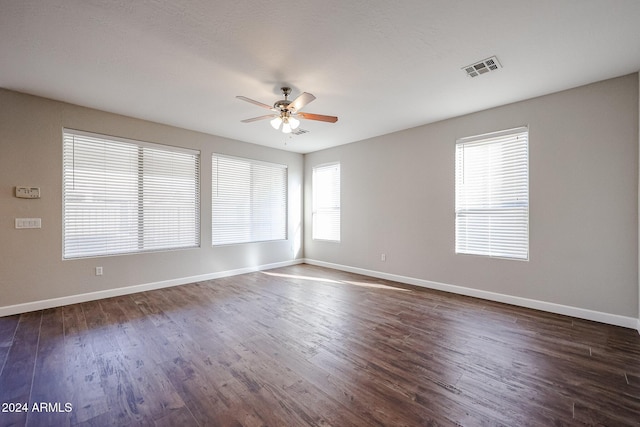 spare room featuring dark wood-type flooring, ceiling fan, and a healthy amount of sunlight