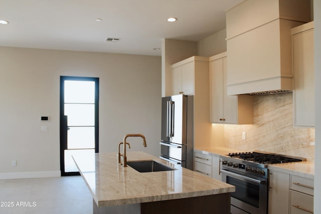 12863 E Cochise Rd, Scottsdale, AZ 85259 - kitchen featuring freestanding refrigerator, high end stainless steel range, decorative backsplash, light stone counters, and a kitchen island with sink