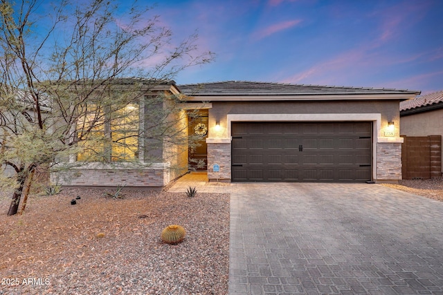 view of front of property with stone siding, decorative driveway, an attached garage, and stucco siding