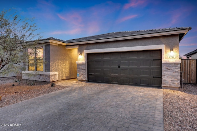 view of front of home featuring decorative driveway, stone siding, an attached garage, and stucco siding