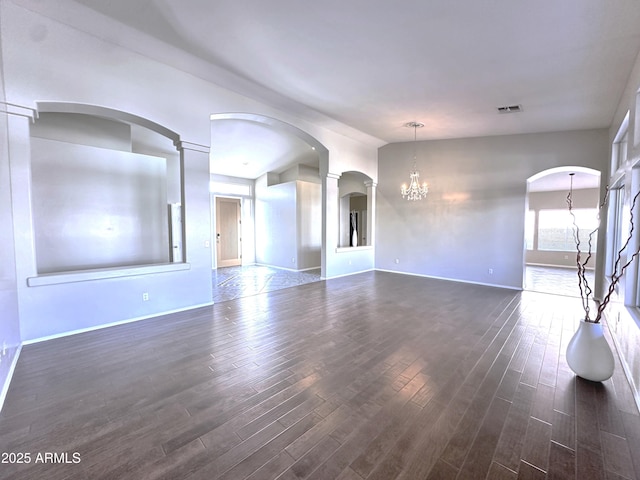 empty room with decorative columns, dark wood-type flooring, and an inviting chandelier