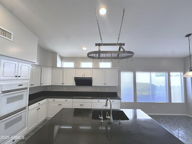 kitchen with sink, white double oven, a healthy amount of sunlight, white cabinets, and cooktop