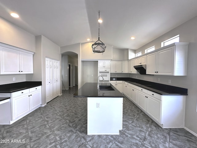 kitchen featuring sink, decorative light fixtures, oven, a kitchen island with sink, and white cabinets