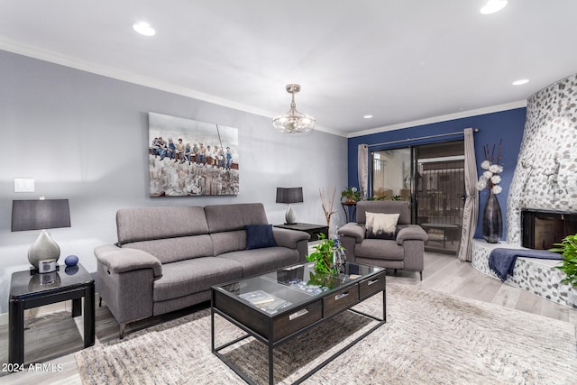 living room featuring ornamental molding, a notable chandelier, a stone fireplace, and light wood-type flooring