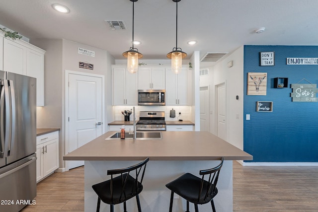 kitchen with an island with sink, white cabinets, decorative backsplash, hanging light fixtures, and stainless steel appliances