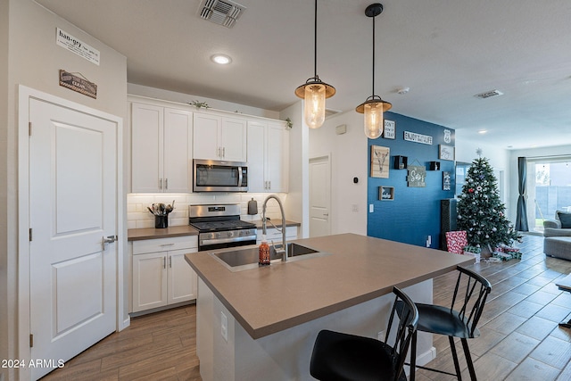 kitchen featuring decorative light fixtures, an island with sink, white cabinets, a kitchen bar, and stainless steel appliances