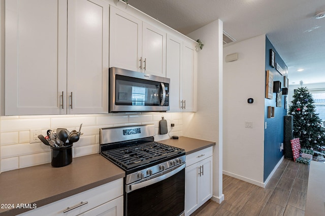 kitchen with backsplash, appliances with stainless steel finishes, hardwood / wood-style flooring, and white cabinets