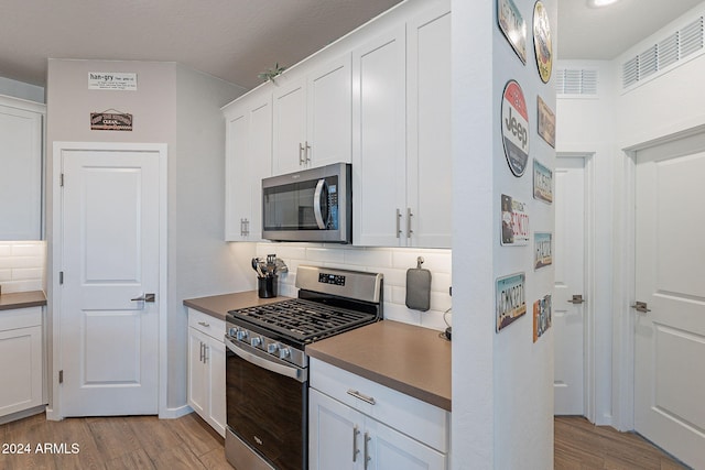 kitchen featuring tasteful backsplash, light wood-type flooring, white cabinets, and appliances with stainless steel finishes