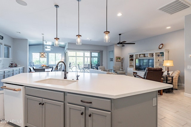 kitchen featuring white dishwasher, hanging light fixtures, a center island with sink, sink, and ceiling fan