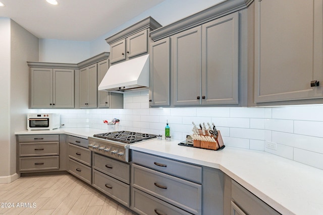 kitchen featuring light hardwood / wood-style floors, stainless steel gas cooktop, tasteful backsplash, custom exhaust hood, and gray cabinets