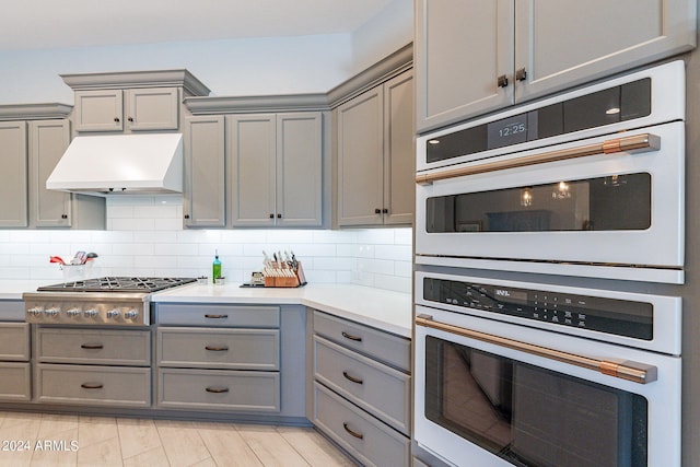 kitchen featuring backsplash, gray cabinetry, custom exhaust hood, and multiple ovens