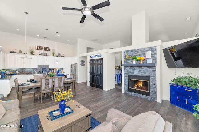 living room with ceiling fan, dark hardwood / wood-style flooring, a towering ceiling, and a stone fireplace