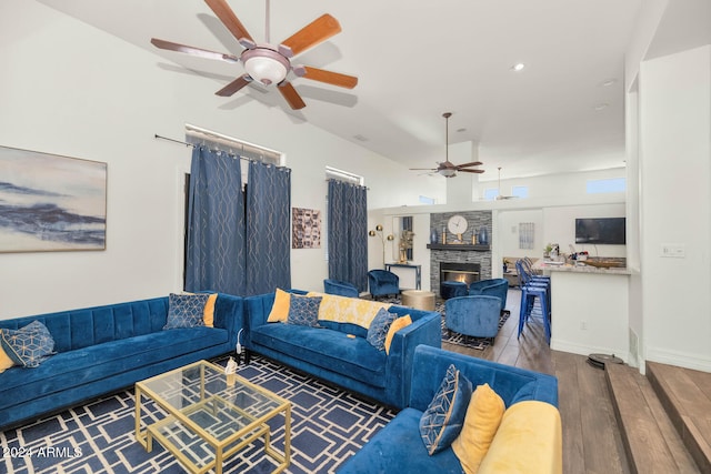 living room with ceiling fan, a stone fireplace, and wood-type flooring