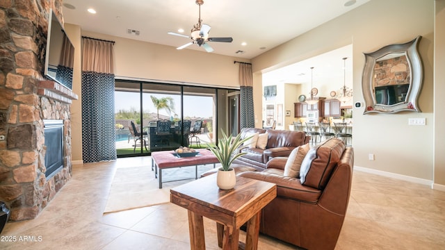 living area with light tile patterned floors, baseboards, visible vents, a ceiling fan, and a stone fireplace