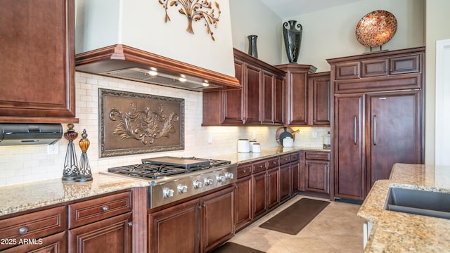 kitchen with light stone counters, custom range hood, stainless steel gas cooktop, and tasteful backsplash