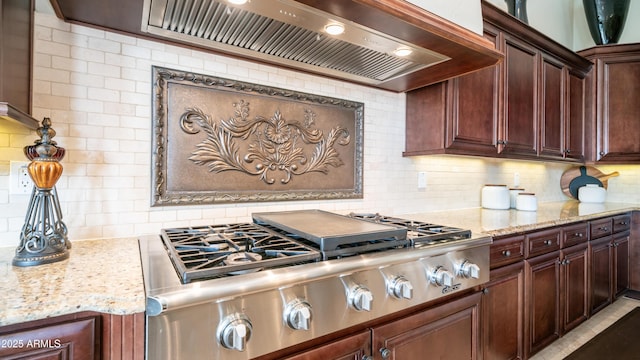 kitchen with light stone counters, premium range hood, stainless steel gas stovetop, and backsplash