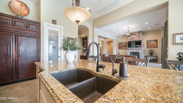 kitchen with light stone counters, arched walkways, a fireplace, visible vents, and a sink