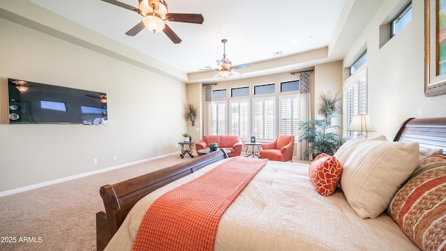 carpeted bedroom with ceiling fan, baseboards, and a raised ceiling