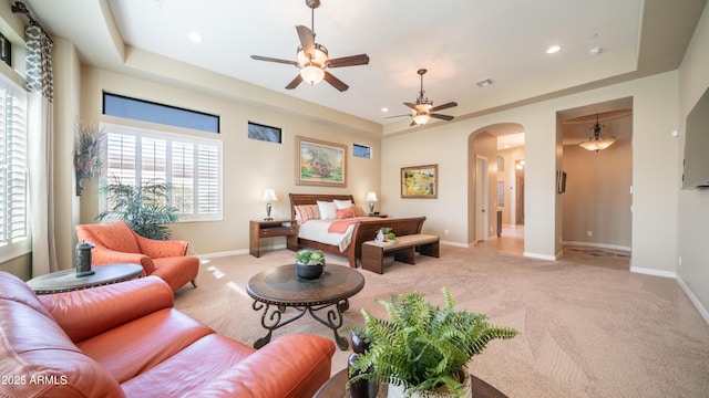 living area with arched walkways, a raised ceiling, and light colored carpet