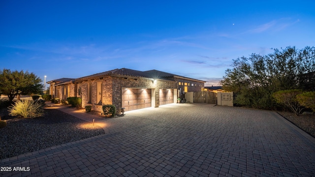 view of front facade with a garage, stone siding, decorative driveway, and a gate